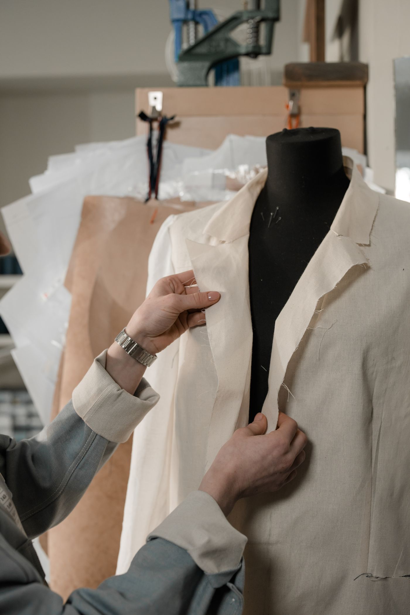Una costurera acomoda la solapa de una chaqueta de lino crudo montada sobre un maniquí negro